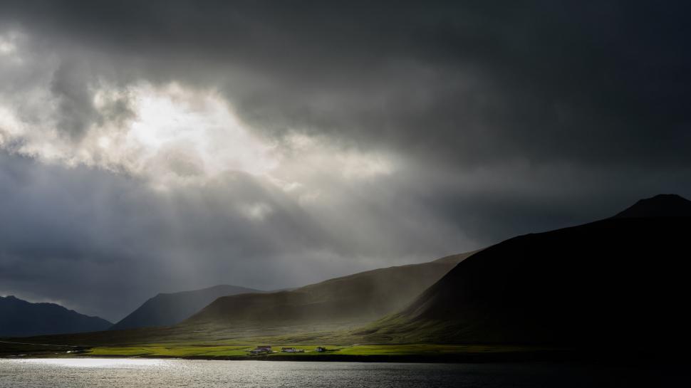 Free Image of Sun rays breaking through dark clouds over green area 