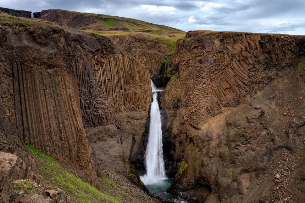 Free Image of Scenic waterfall flowing between rugged rocky cliffs 