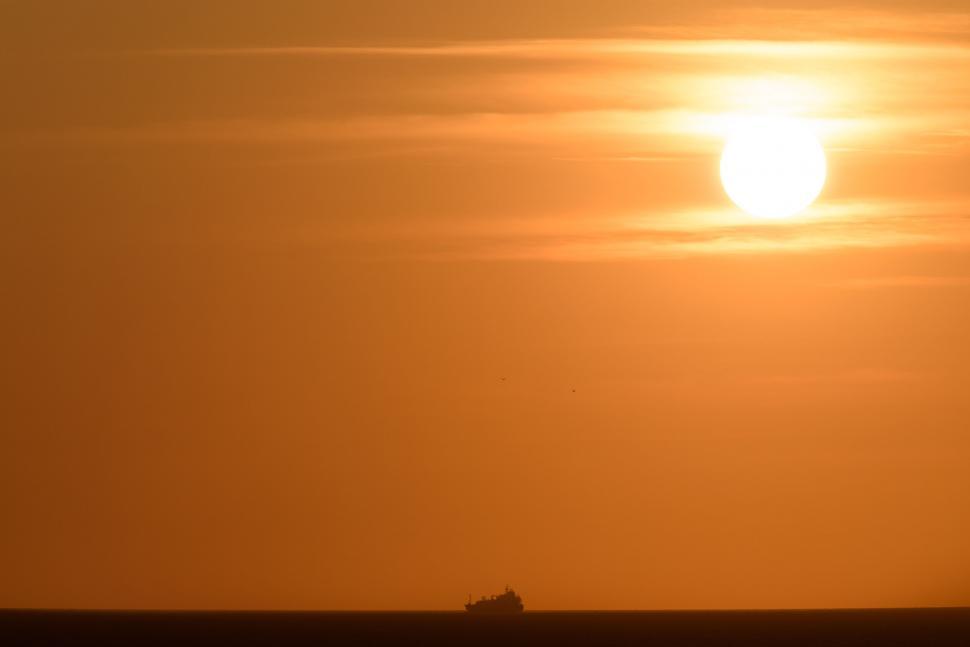 Free Image of Sunset over the ocean with a distant ship silhouette 