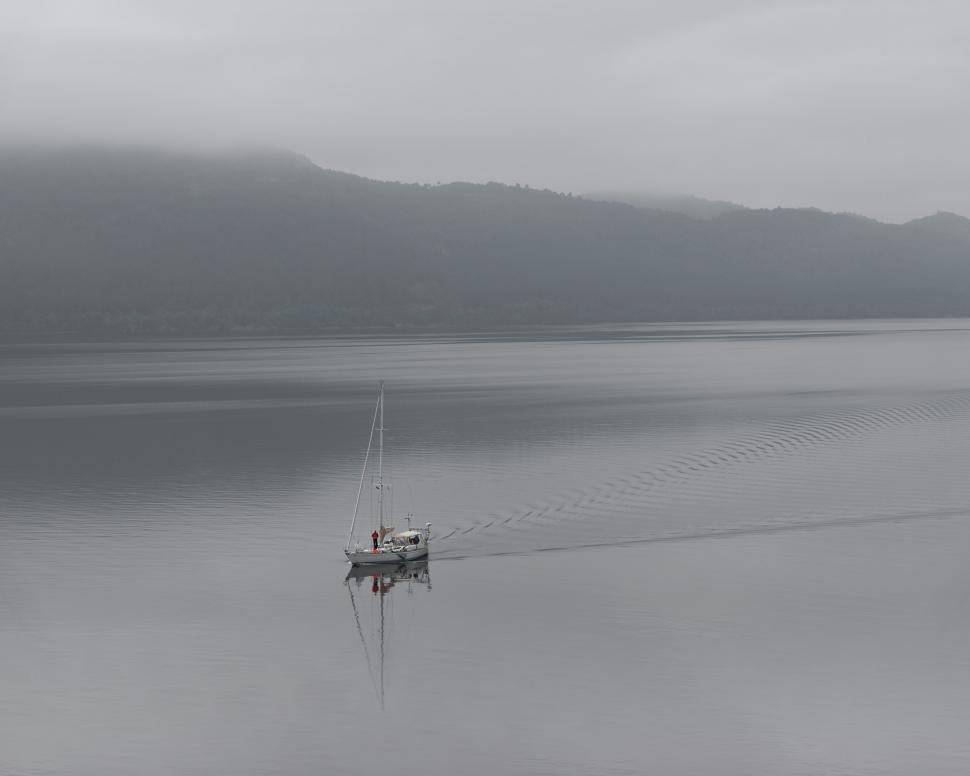 Free Image of Sailboat moving across calm lake on a foggy day 