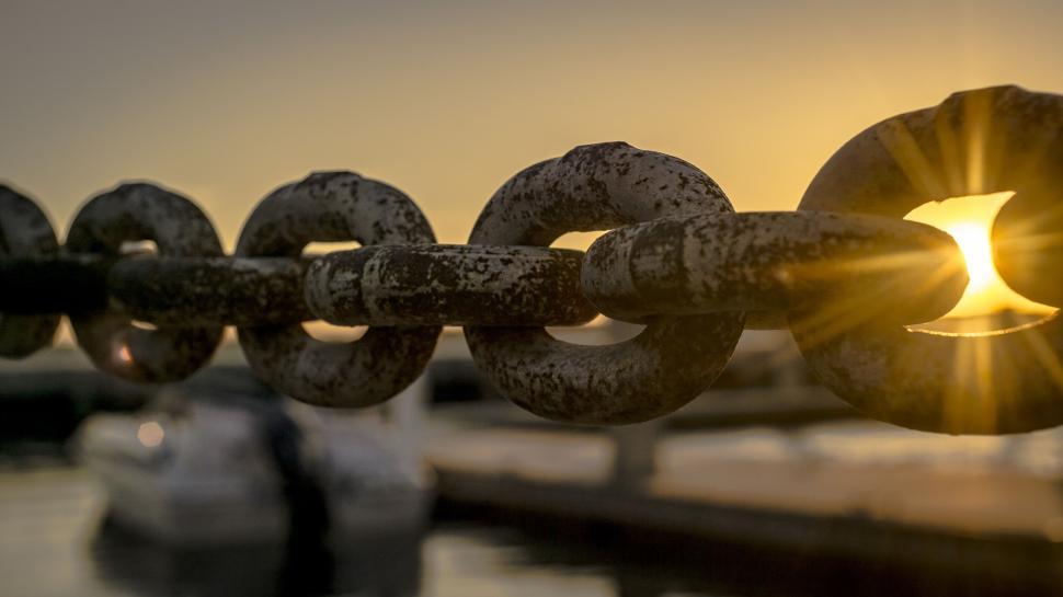 Free Image of Sunset reflecting through chain link at a marina. 