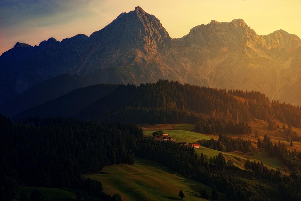 Free Image of Sunlit mountain range with dense trees and small houses. 