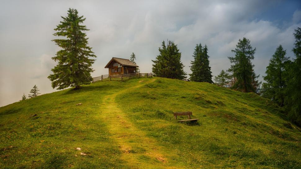 Free Image of Rustic cabin on a green hill with a surrounding fence. 