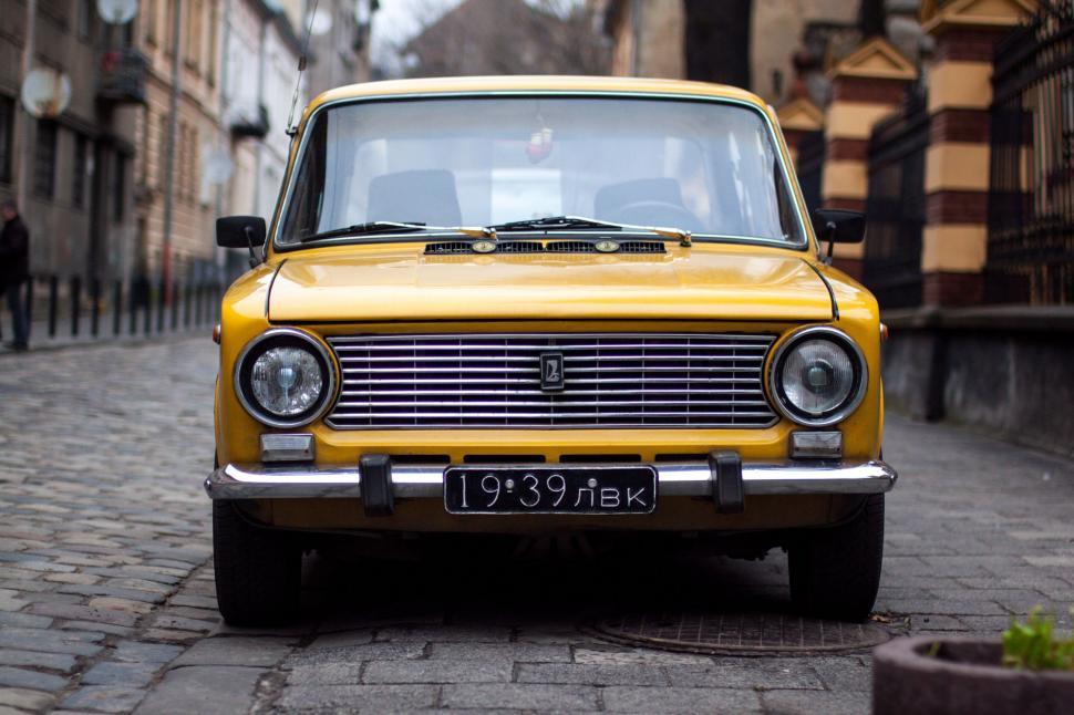 Free Image of Yellow vintage car parked on a cobbled street 