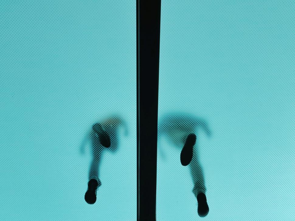 Free Image of Silhouetted people walking on glass floor against blue light. 