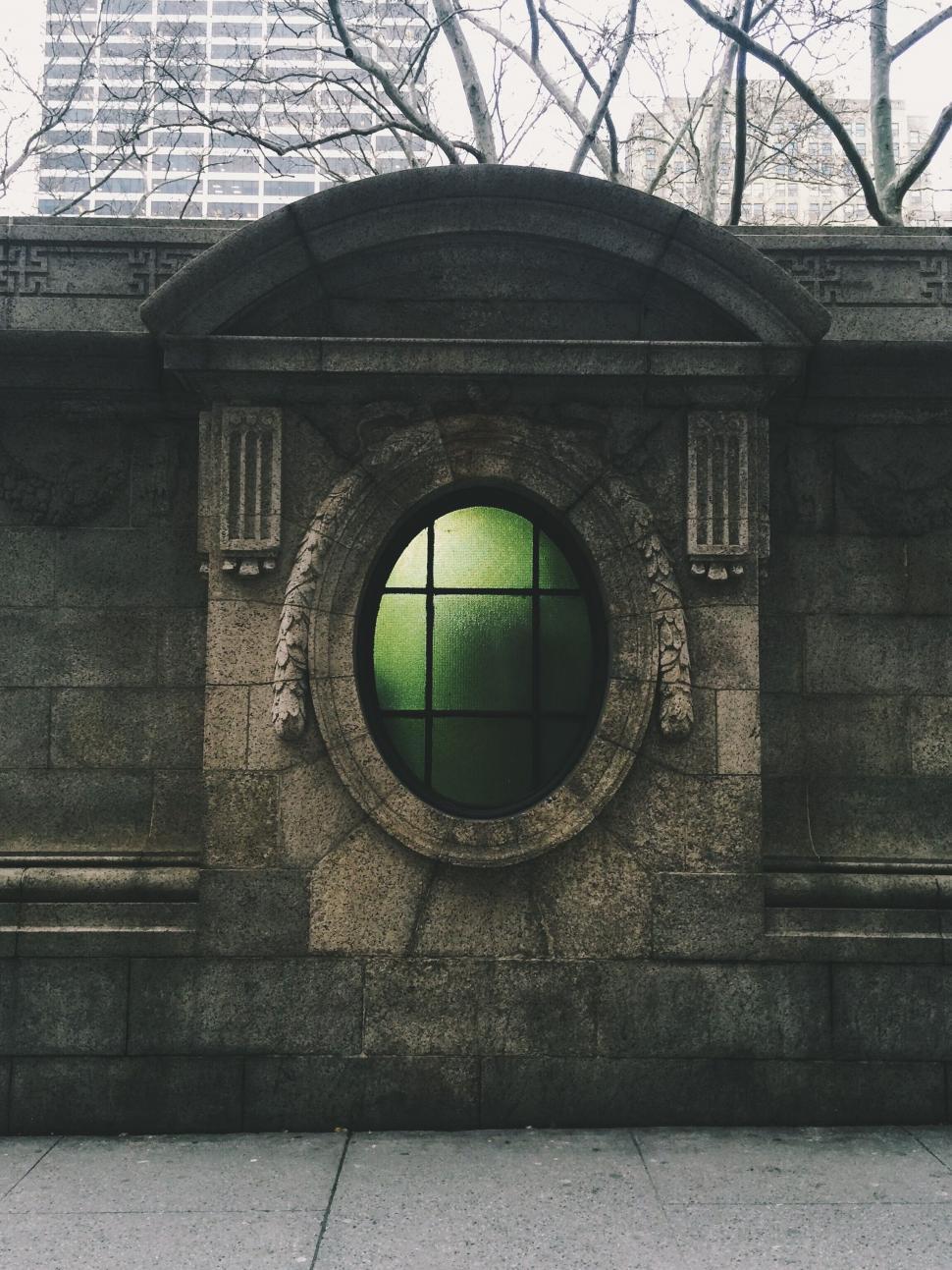 Free Image of Stone wall with oval green window in urban setting view 