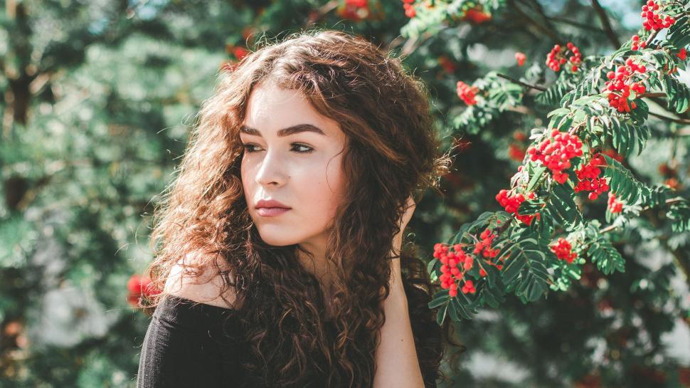 Free Image of Woman with curly hair standing near vibrant red berries. 