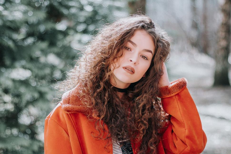 Free Image of Person with curly hair in orange coat in forest. 