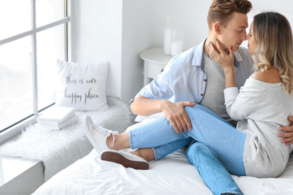 Affectionate couple sitting on the bed in a brightly lit bedroom.