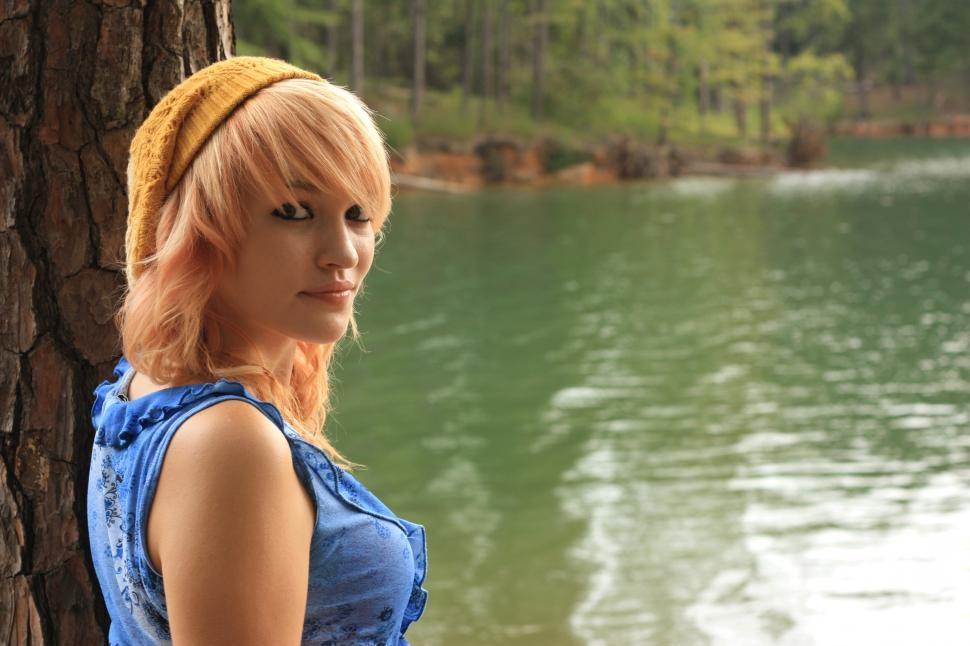 Free Image of A beautiful young woman posing against a tree by a lake 