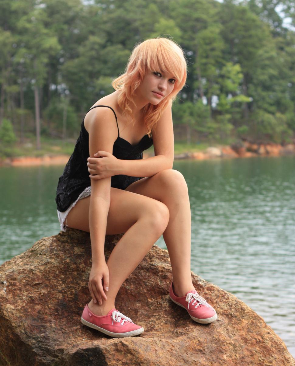 Free Image of A beautiful young woman posing on a rock by a lake 