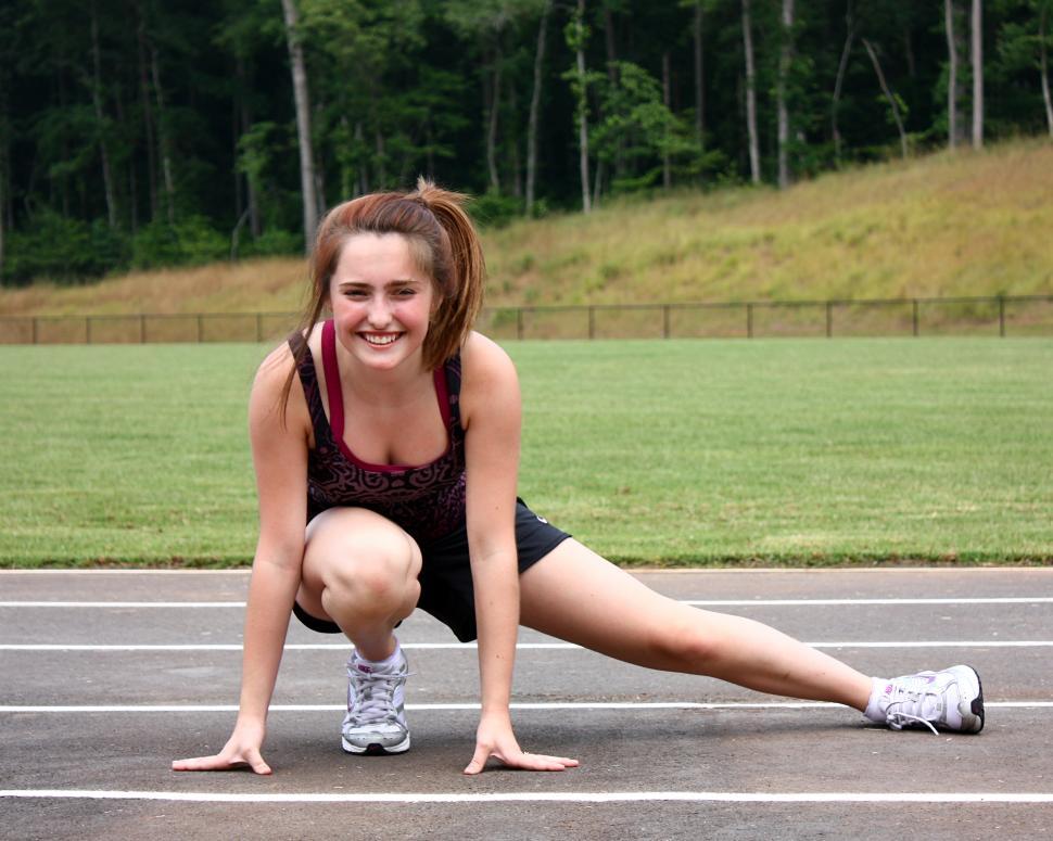Free Image of A cute young girl doing stretches on a track field 