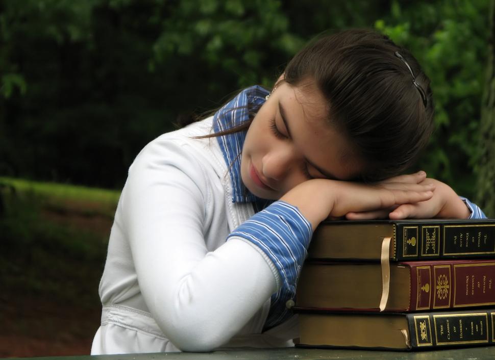 Free Image of A young schoolgirl resting her head on a stack of books 