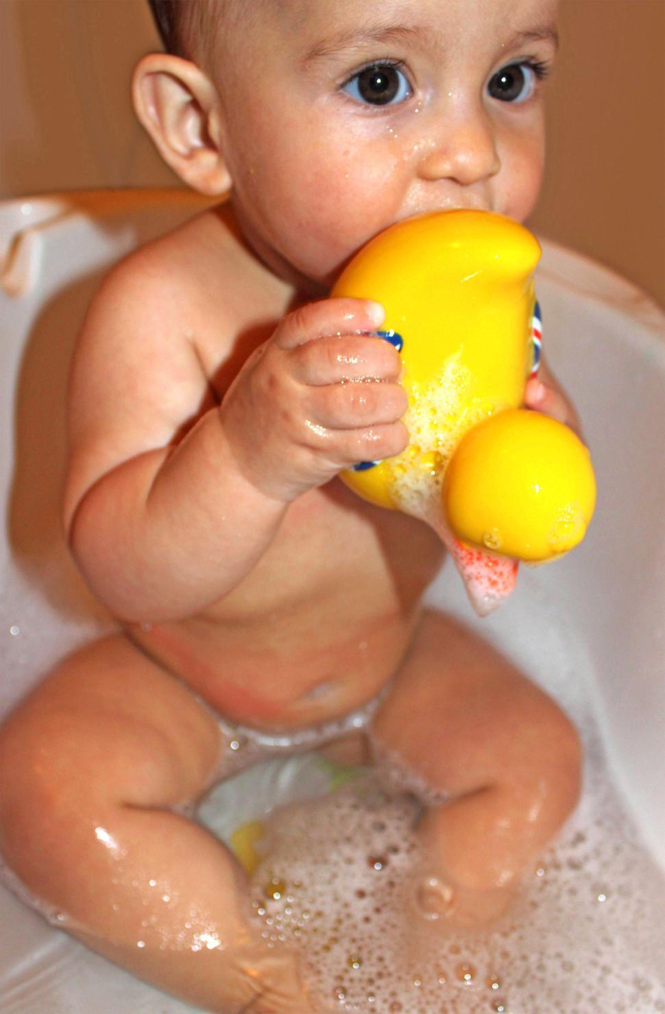 Free Image of Baby bathing while holding and suckling a yellow duck toy 