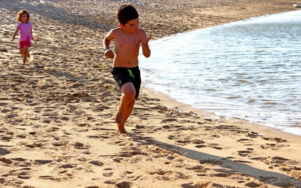 Free Image of A little boy and a little girl running on the beach 