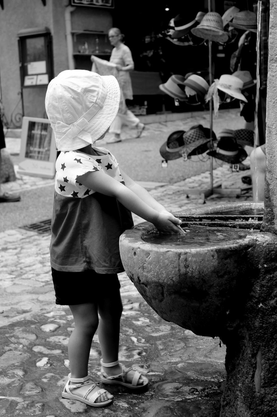 Free Image of Toddler washing her hands while observing hats for sale in Moust 