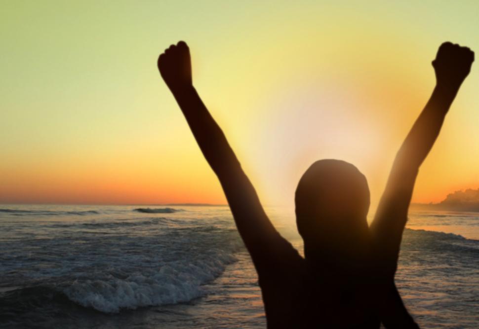 Free Image of Woman with arms raised at sunset on the beach 