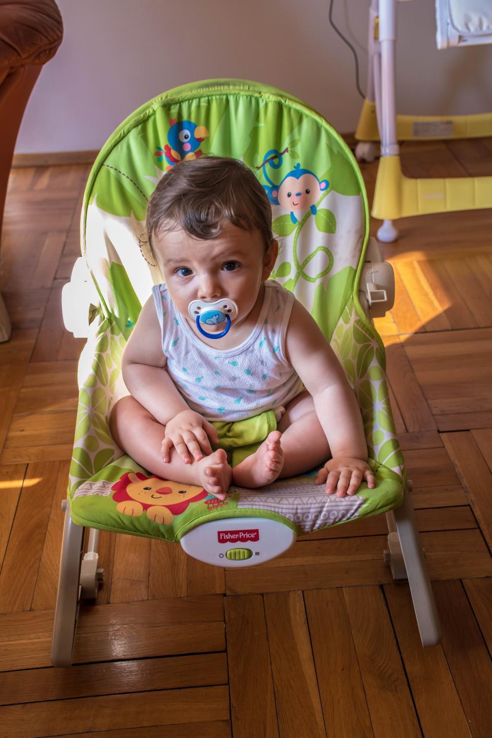 Free Image of Baby Sitting in High Chair With Pacifier 