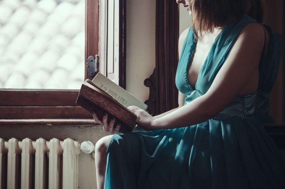 Free Image of Woman Sitting on Window Sill Reading a Book 