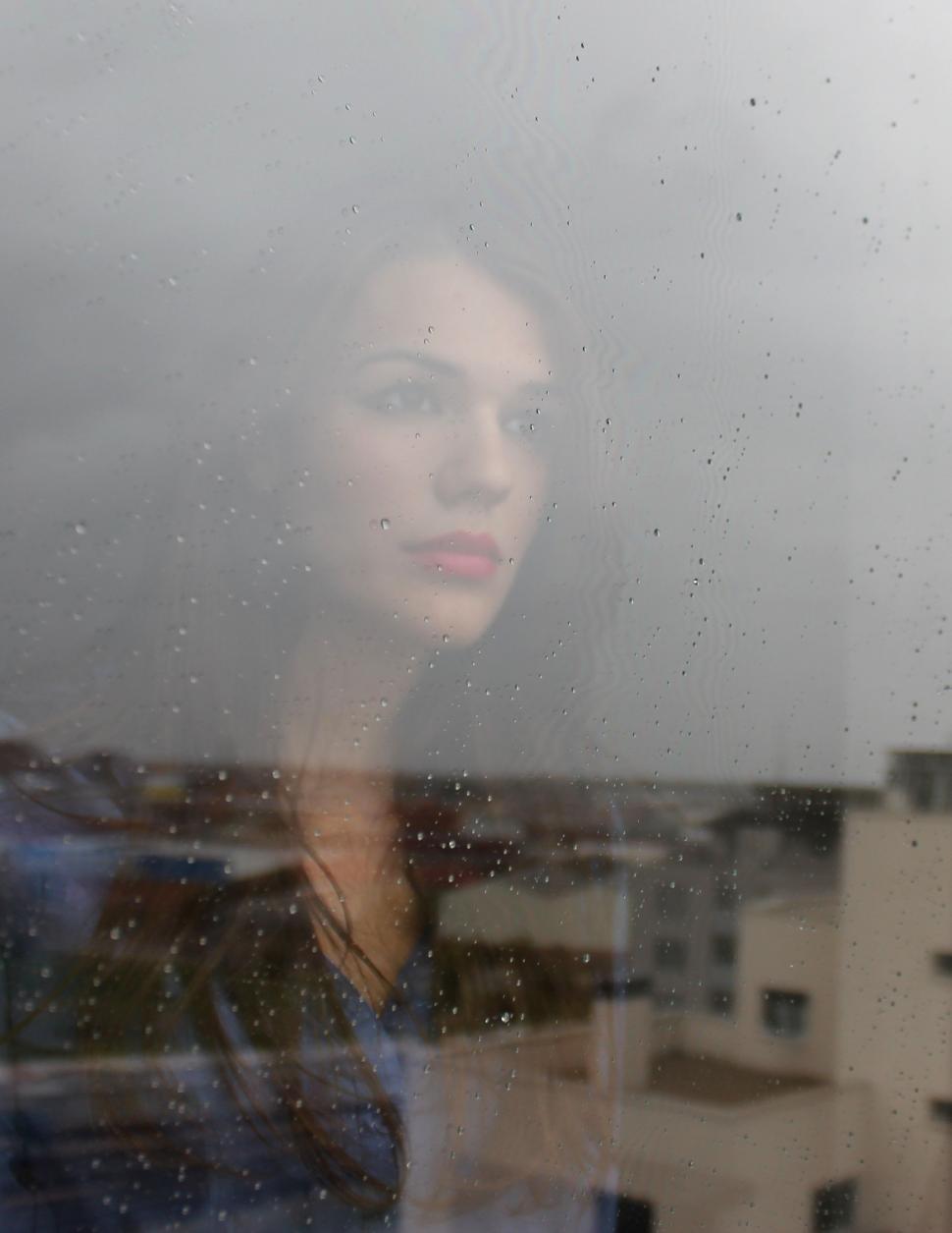 Free Image of Woman Looking Out of Window With Building in Background 