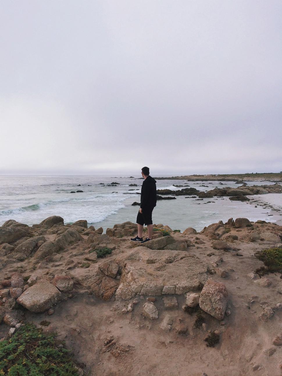 Free Image of Man Standing on Rocky Beach by Ocean 