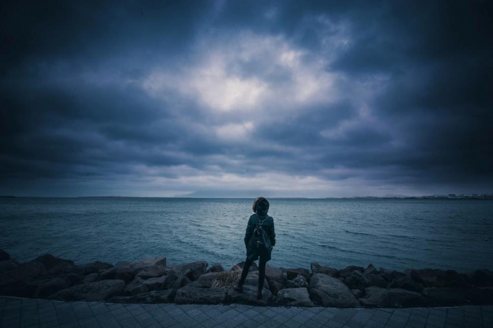 Free Image of Person Standing on Rocks by Ocean Under Cloudy Sky 
