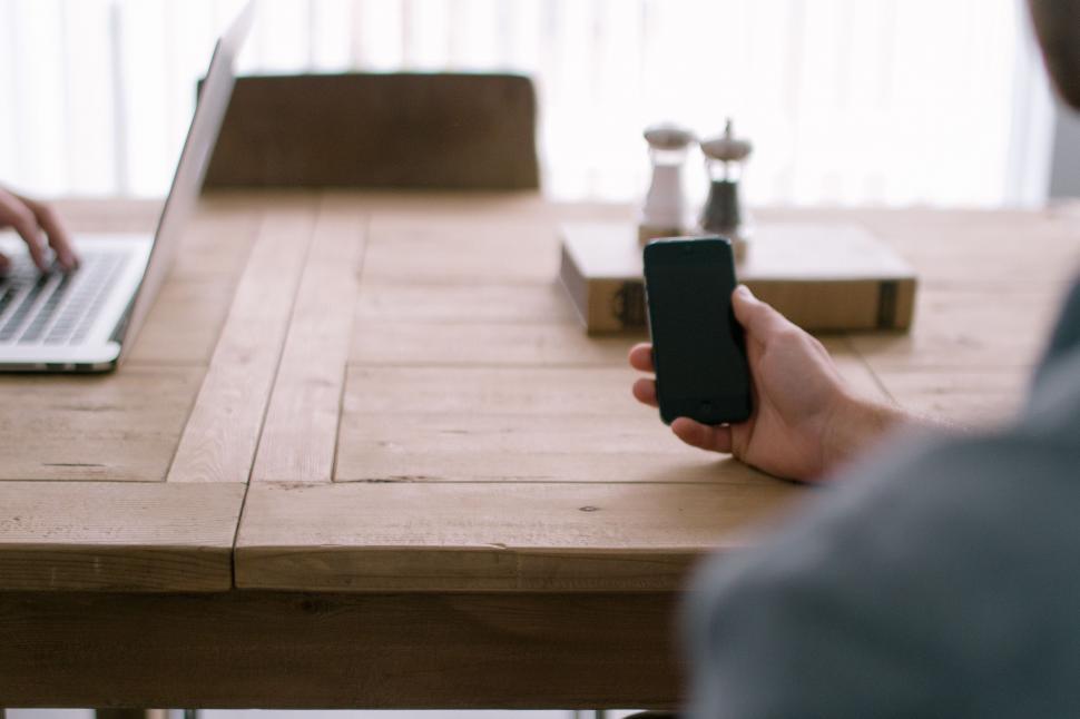 Free Image of Person Sitting at Table Using Cell Phone 