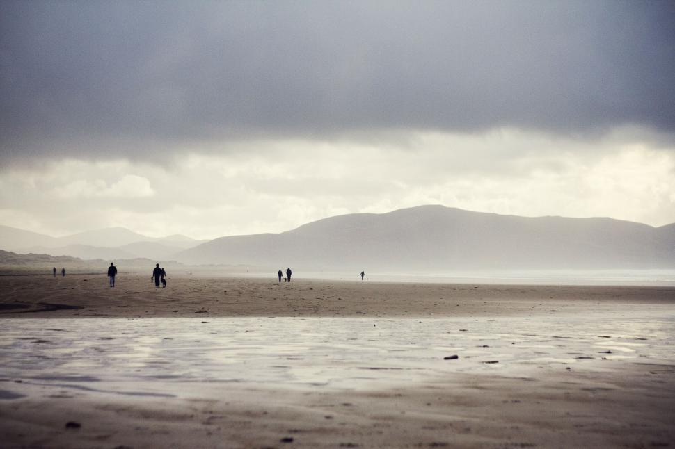 Free Image of Group of People Walking Across Beach Under Cloudy Sky 