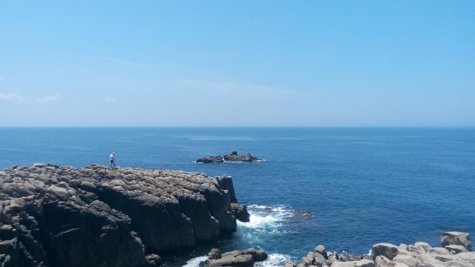 Free Image of Person Standing on Rocky Outcropping by the Ocean 