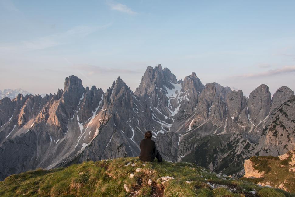 Free Image of Person Sitting on Top of Hill With Mountains in Background 