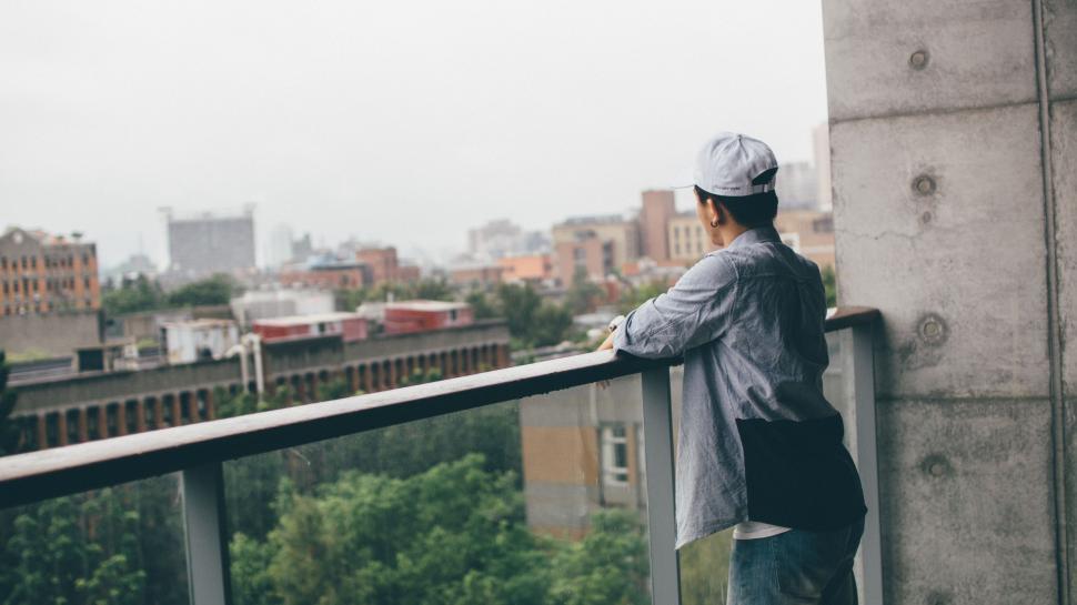 Free Image of Man Standing on Balcony Beside Tall Building 