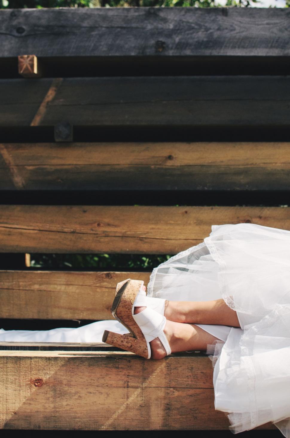 Free Image of Woman in White Dress Laying on Wooden Bench 