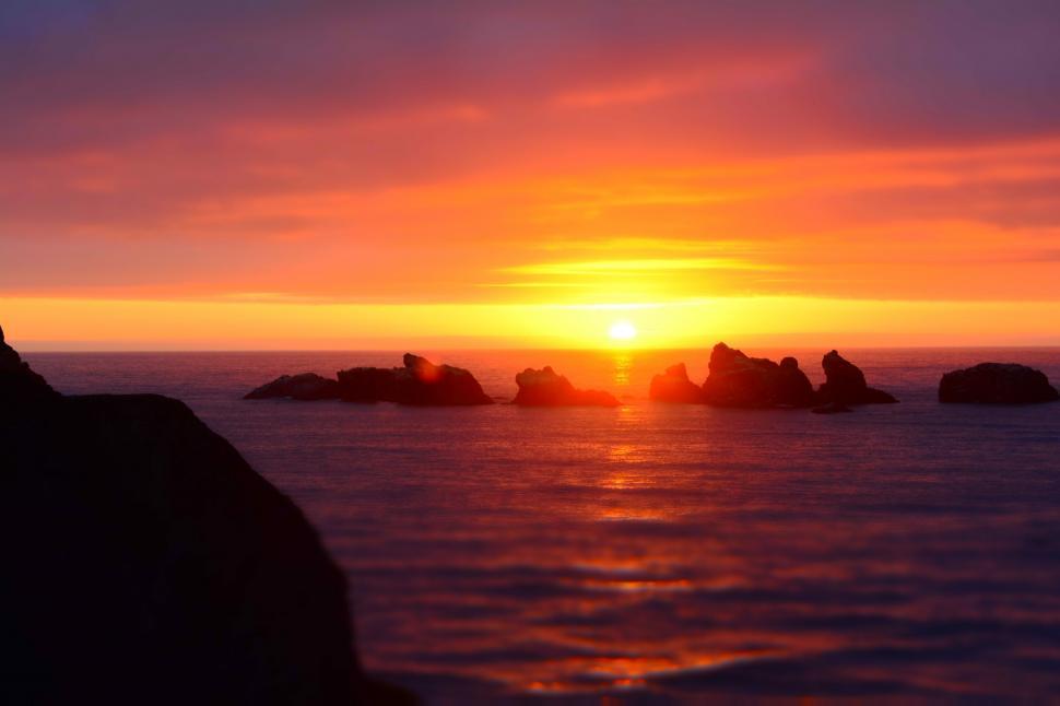 Free Image of Sunset Over Body of Water With Foreground Rocks 