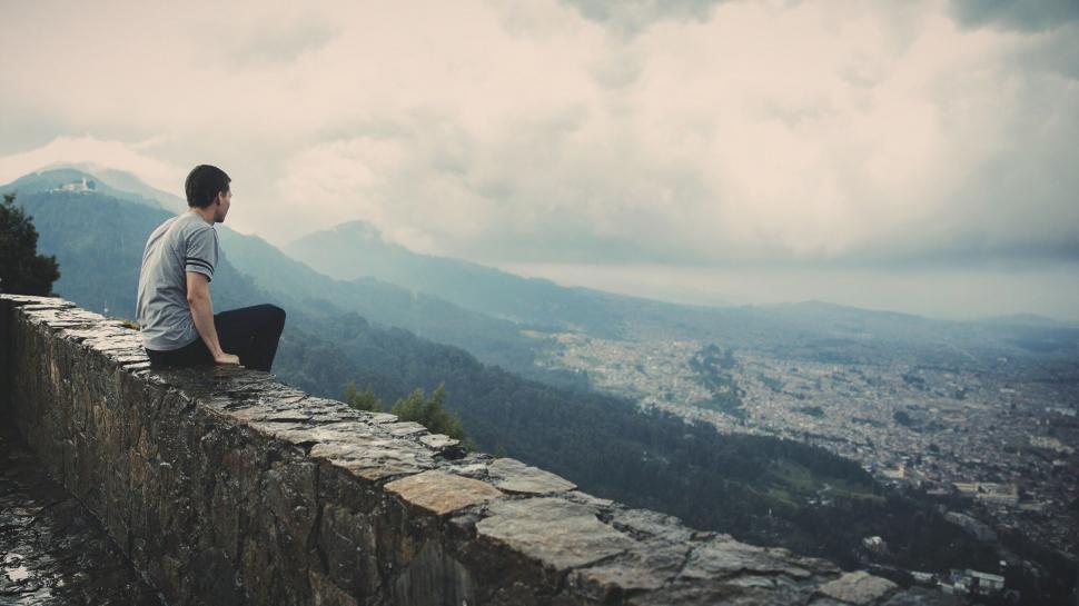 Free Image of Man Sitting on Top of Stone Wall 