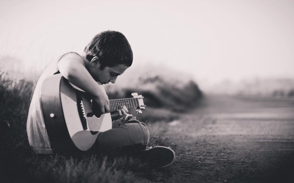 Free Image of Boy Sitting in Field Playing Guitar 