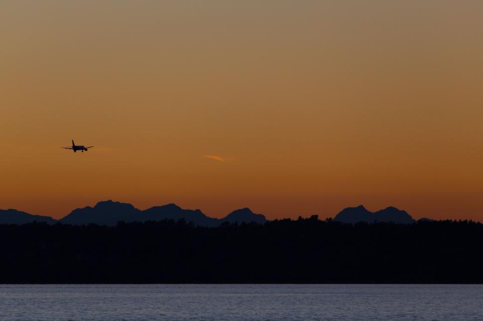 Free Image of Plane Flying Over Body of Water at Sunset 