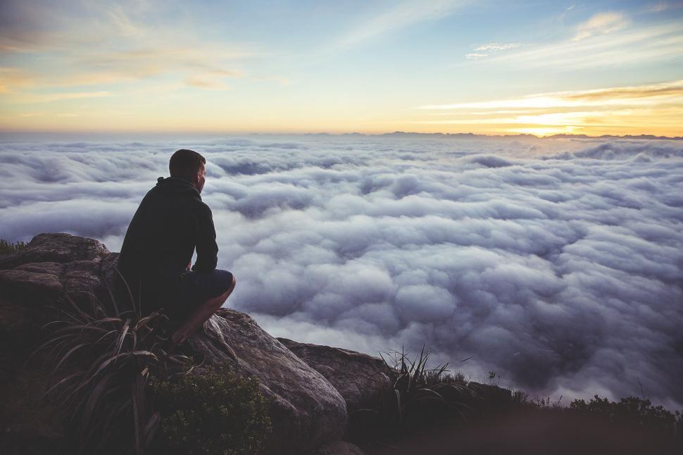 Free Image of Man Sits Atop Mountain Above Clouds 