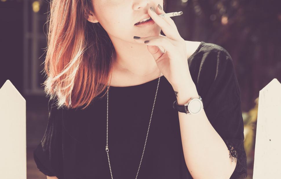 Free Image of Woman Smoking Cigarette in Front of Fence 