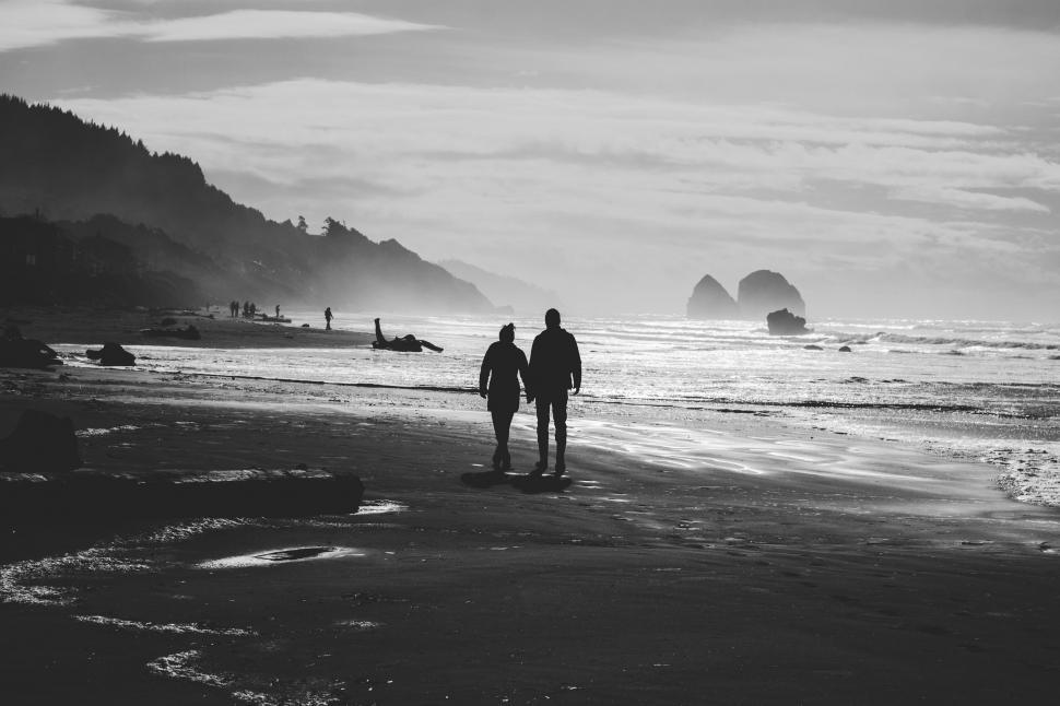 Free Image of Two People Walking on a Beach Near the Ocean 