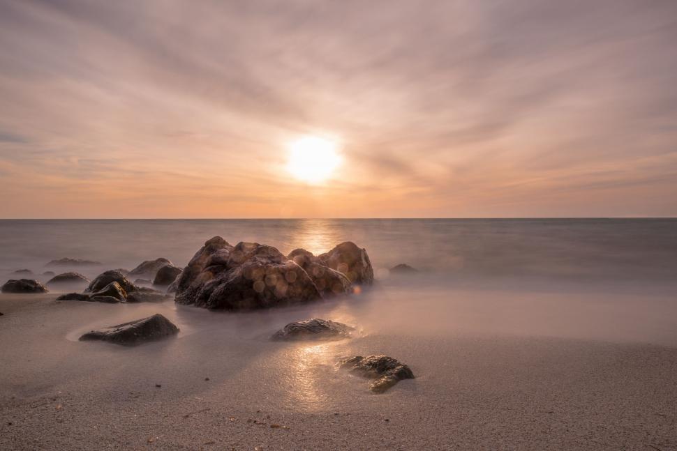 Free Image of Sun Setting Over Ocean With Rocks in Foreground 