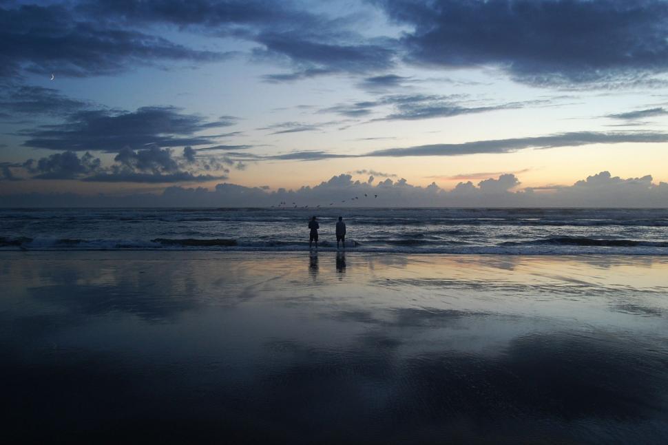 Free Image of Couple Standing on Beach Under Cloudy Sky 