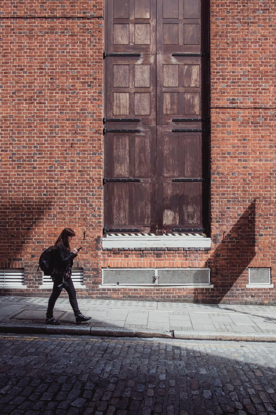 Free Image of Woman Walking Past Tall Brick Building 