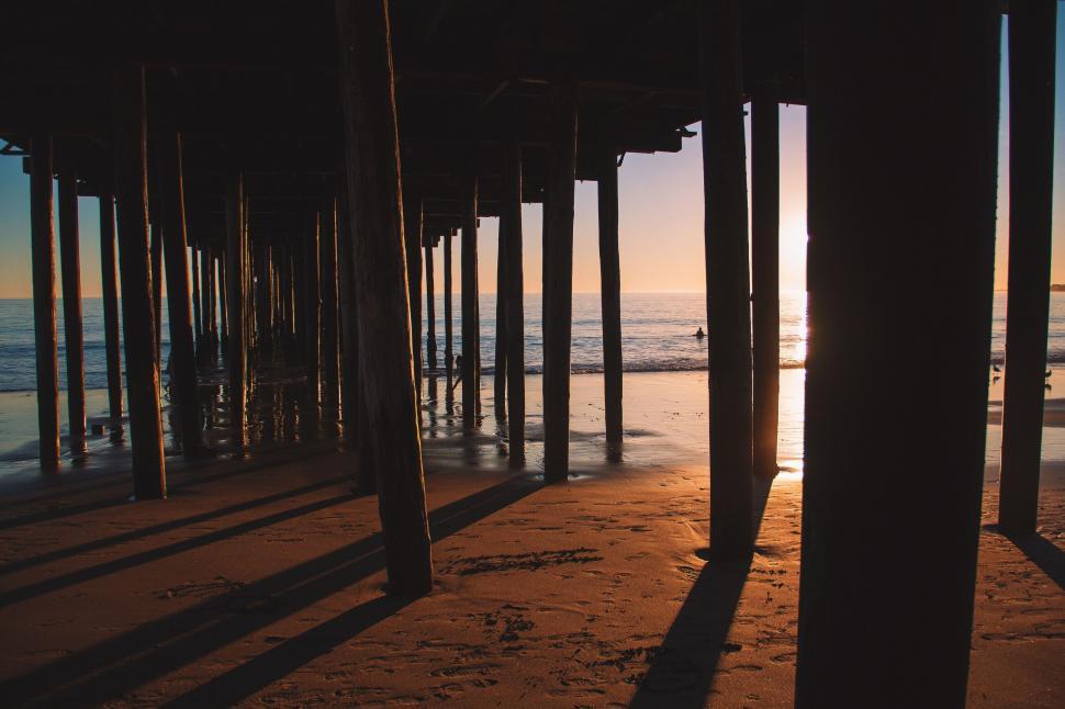 Free Image of The Sun Sets Behind a Pier on the Beach 