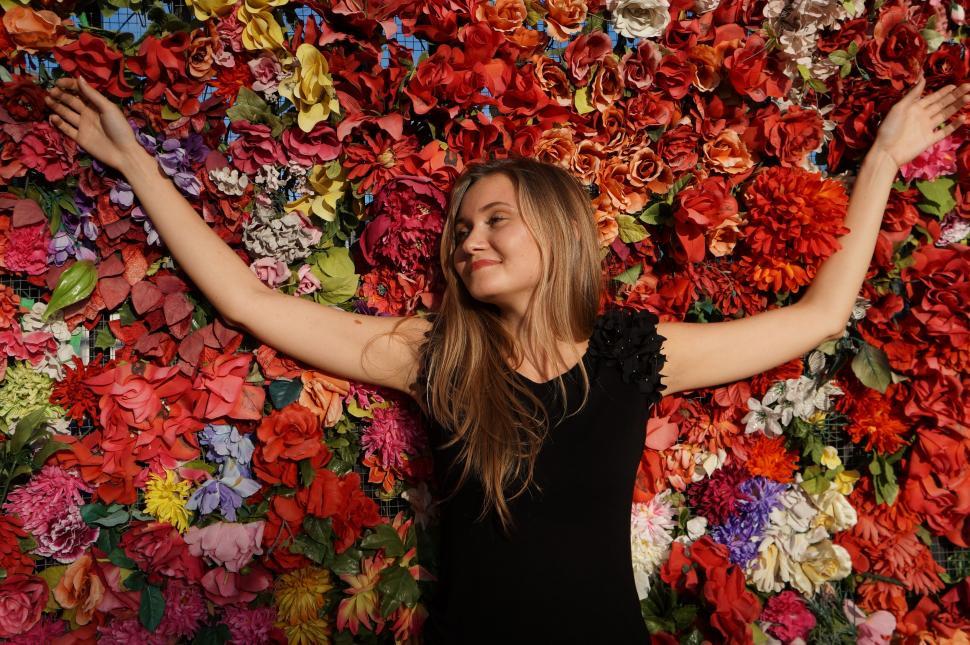 Free Image of Woman Standing in Front of Wall of Flowers 