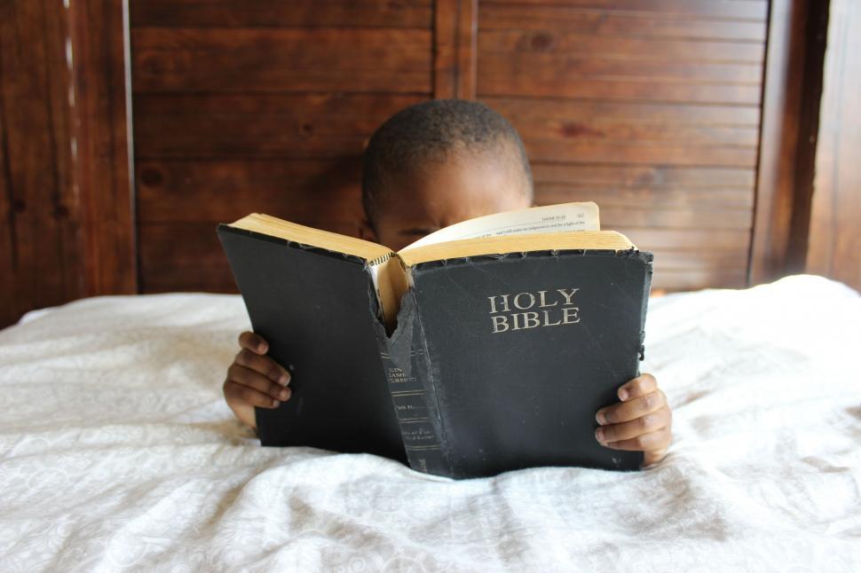 Free Image of Young Boy Reading Bible on Bed 