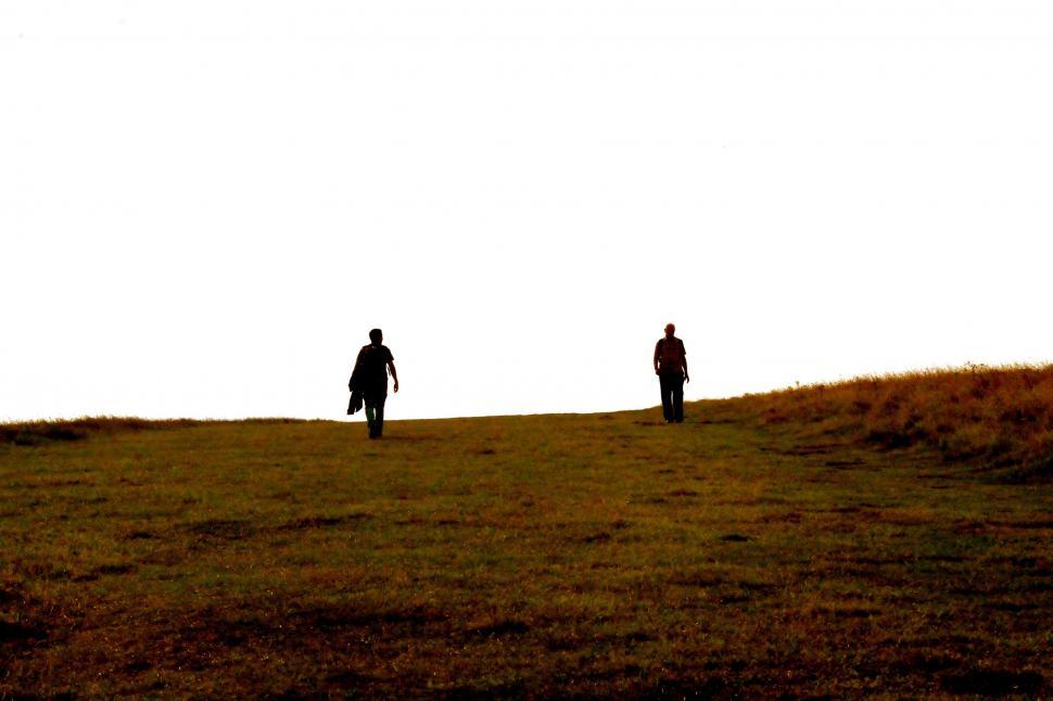 Free Image of Two People Walking Across a Grass Covered Field 