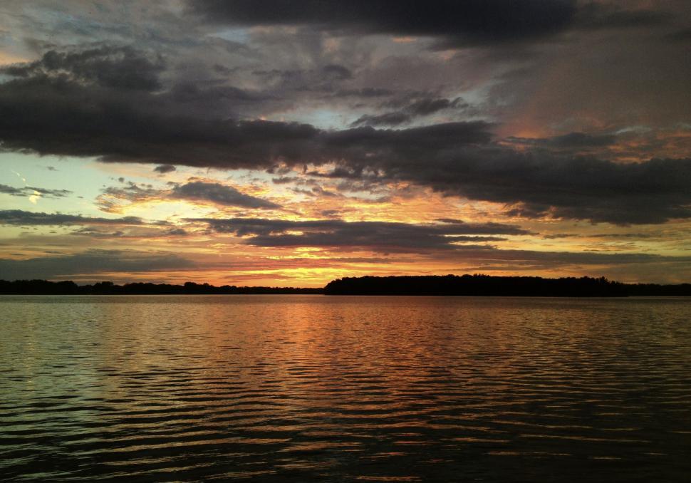 Free Image of Sun Sets Over Water With Clouds in Sky 