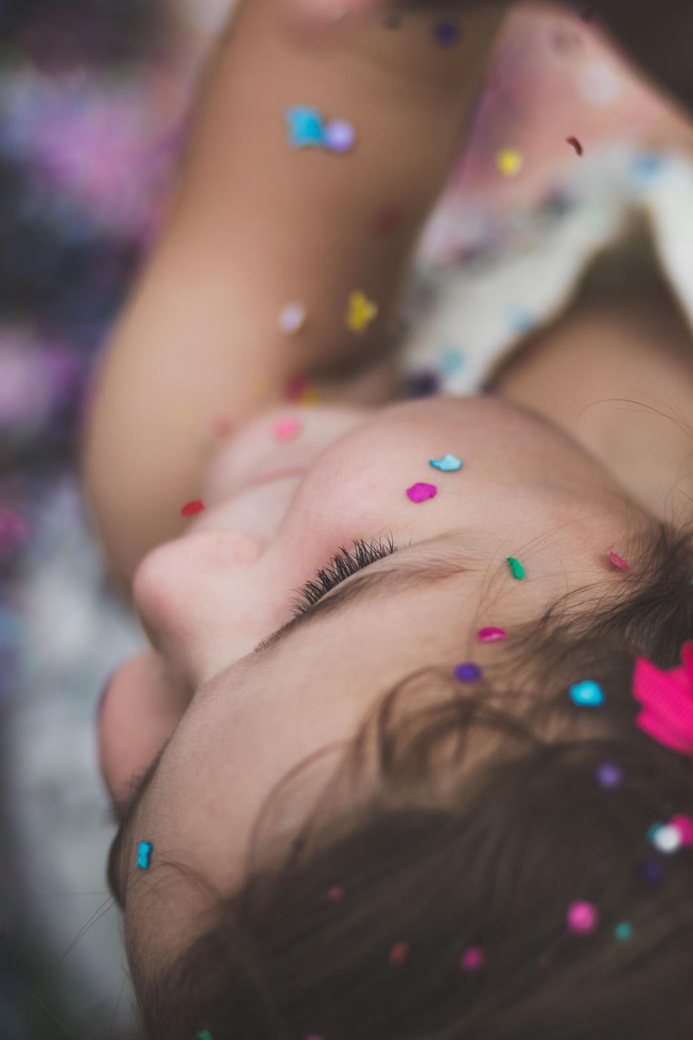 Free Image of Little Girl Laying on Bed Covered in Confetti 