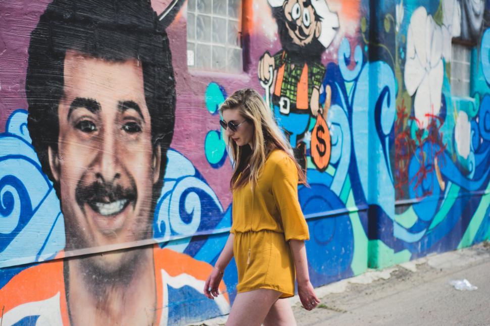 Free Image of Woman Walking Past Wall With Painting of Man 