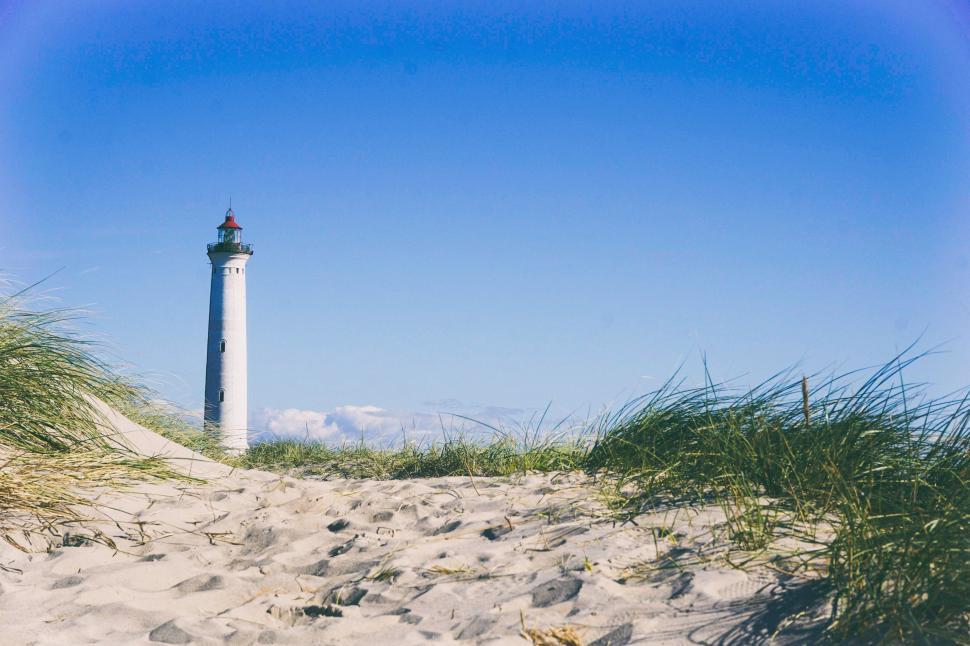 Free Image of Lighthouse Standing on Sandy Beach With Grass in Foreground 